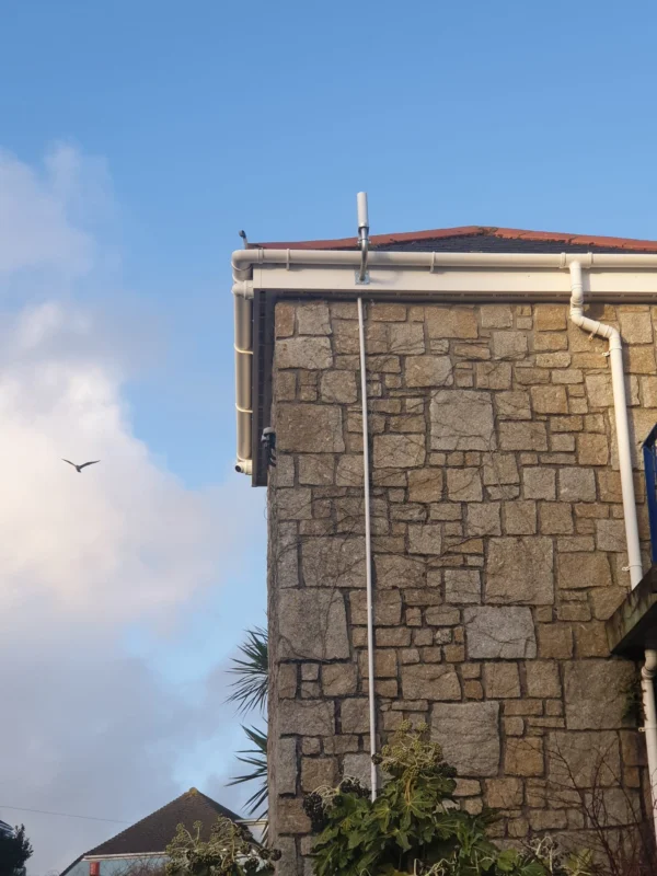 Aerial installed on the side of a stone-walled house with clear blue sky in the background.