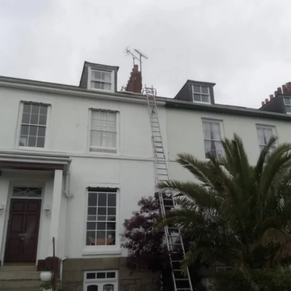 A long ladder leading to a rooftop with a TV aerial installed on the chimney of a multi-storey house.